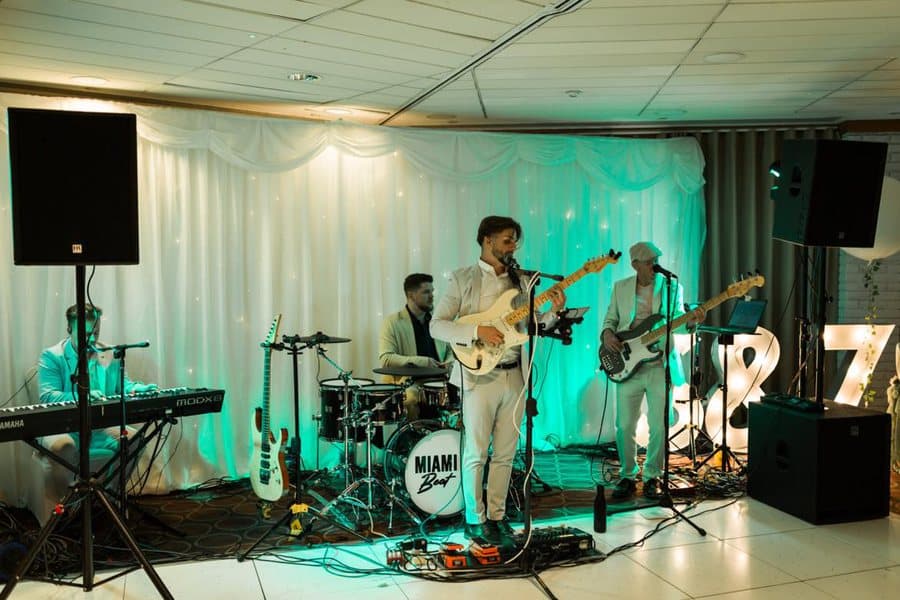 Miami Beat playing at the Abbey Hotel, the stage lit teal beside a light-up display